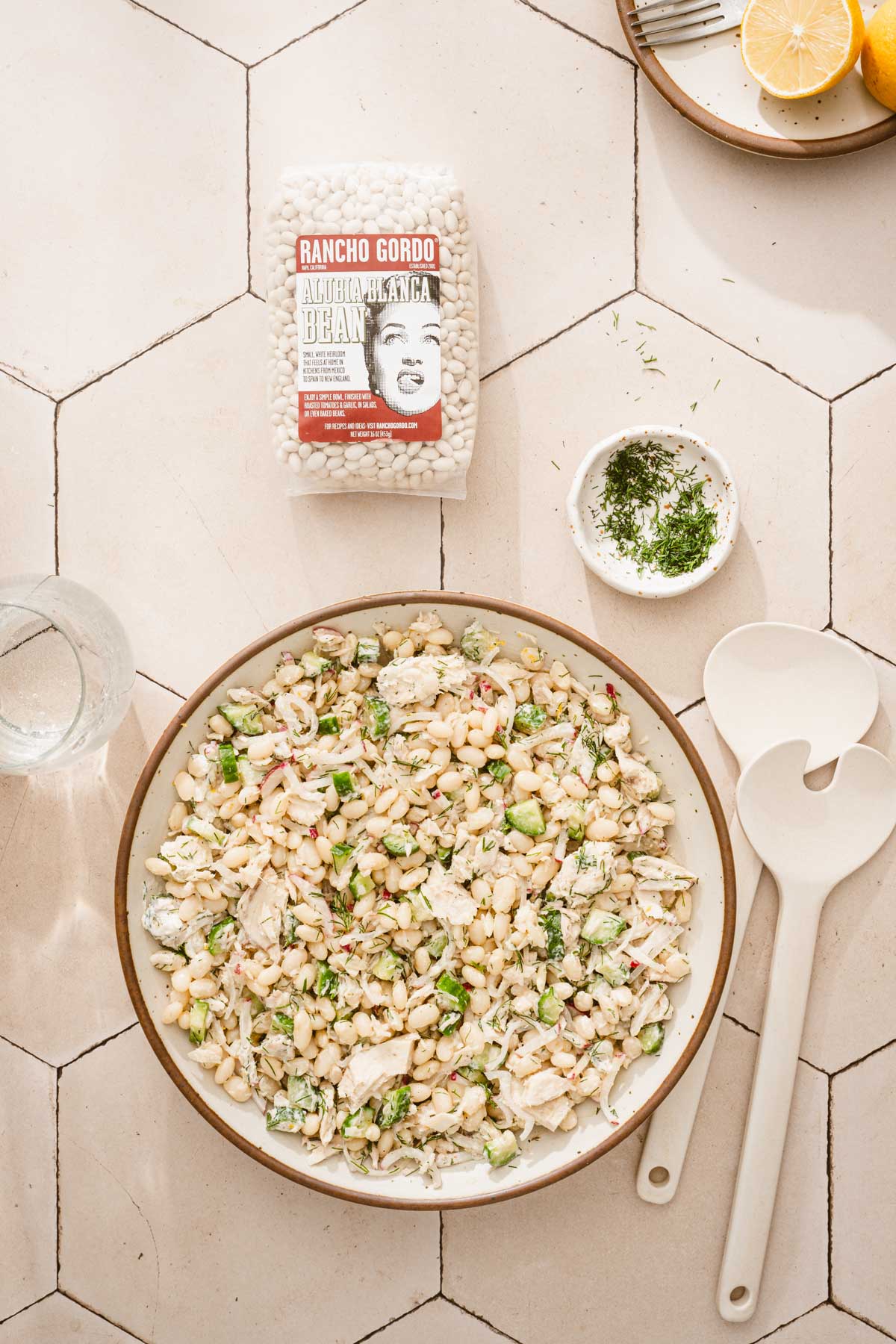 largew serving bowl with white bean salad, bag with dry beans, plats with forks, serving utnsils, dish with dill
