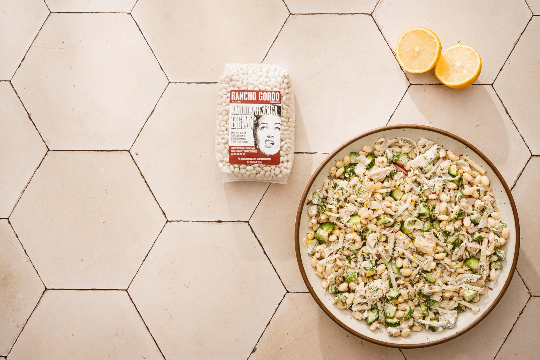 horizontal ratio image of large bowl with the white bean salad, lemon