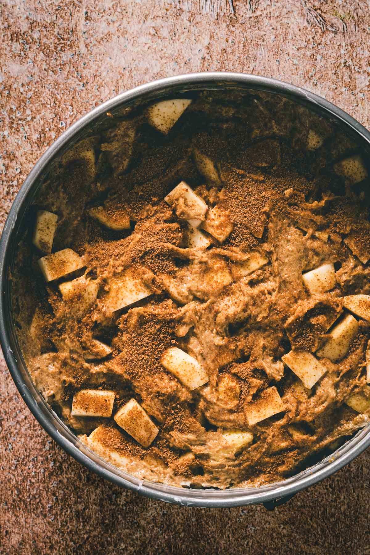 One-bowl apple cake batter in a springform pan, sprinkled with cinnamon sugar topping before baking.