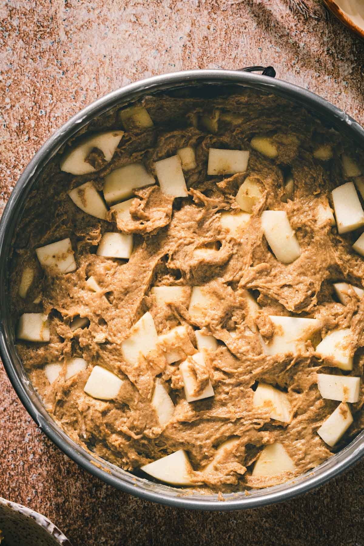 Spiced brown butter cake batter spread in a springform pan with chunks of fresh peeled apple on top.
