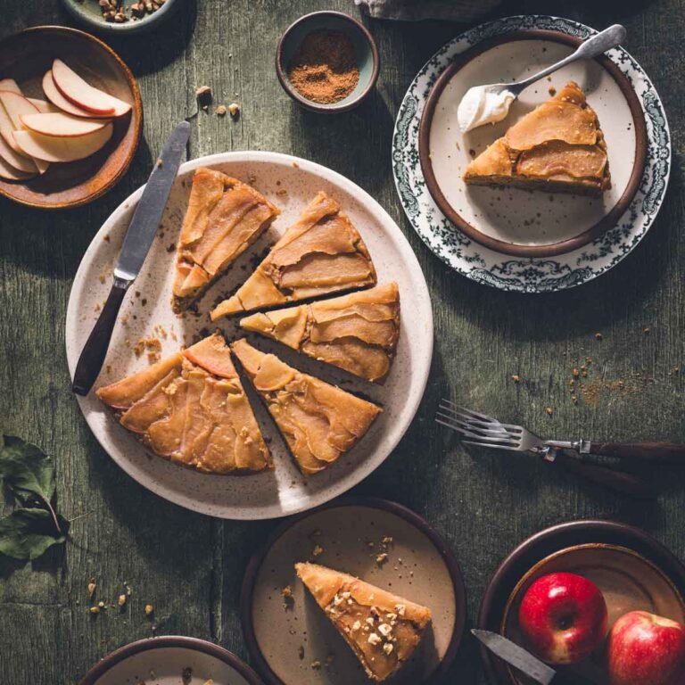 Sliced apple upside down cake on a platter with servings on small plates, including a vintage green transferware plate.