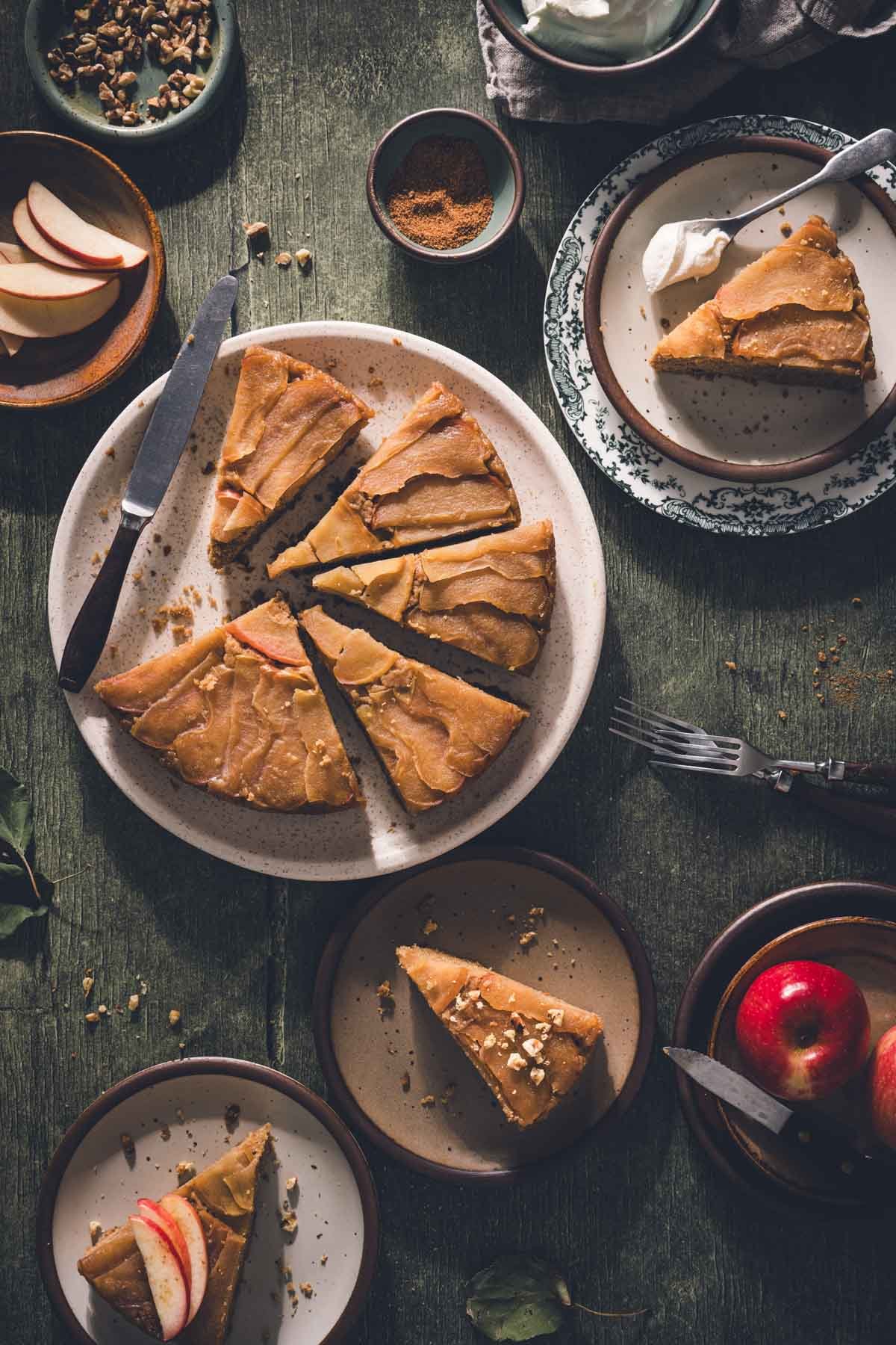 Sliced apple upside down cake on a platter with servings on small plates, including a vintage green transferware plate.