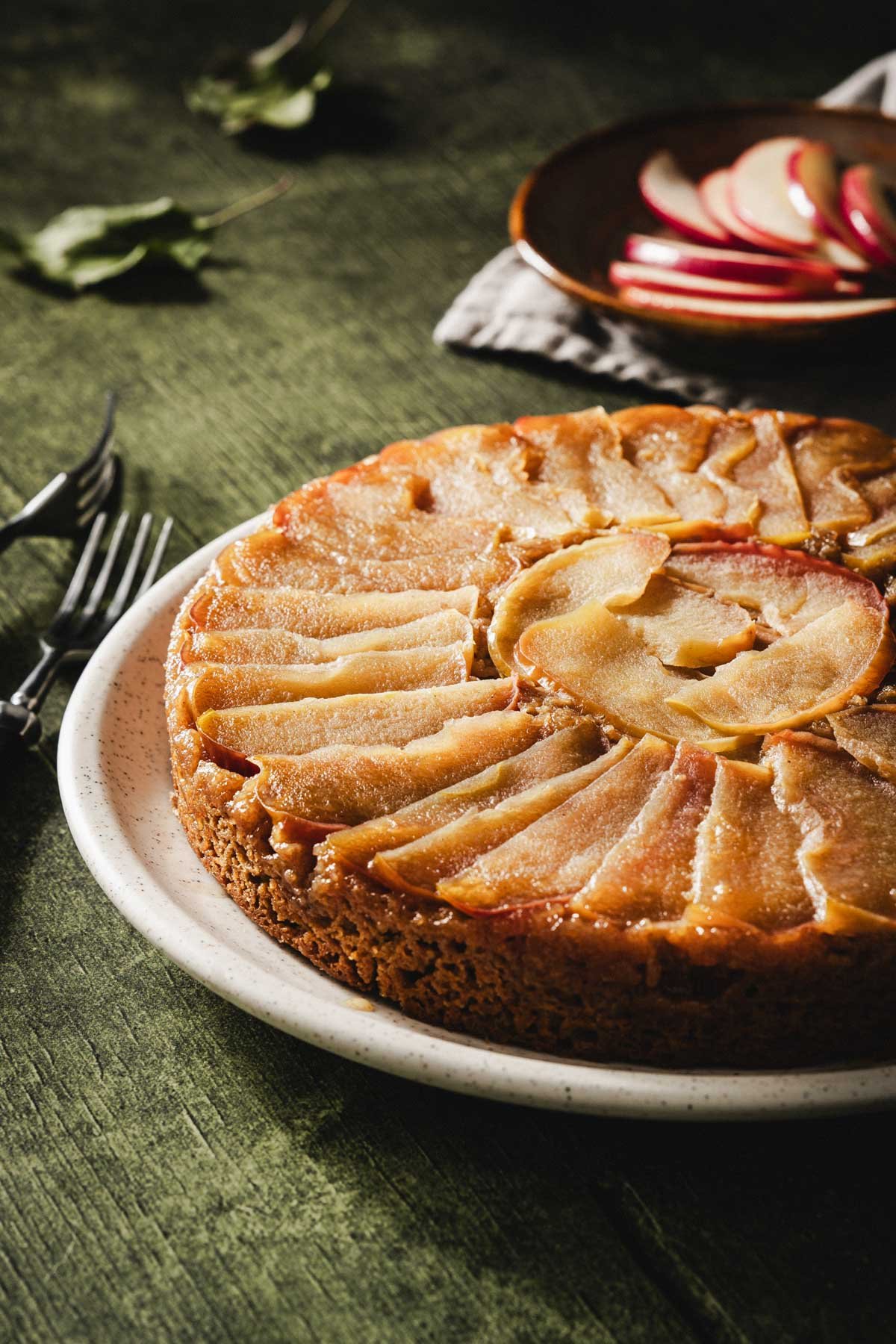 Close-up of whole apple upside down cake with a caramelized apple spiral topping on a speckled platter.