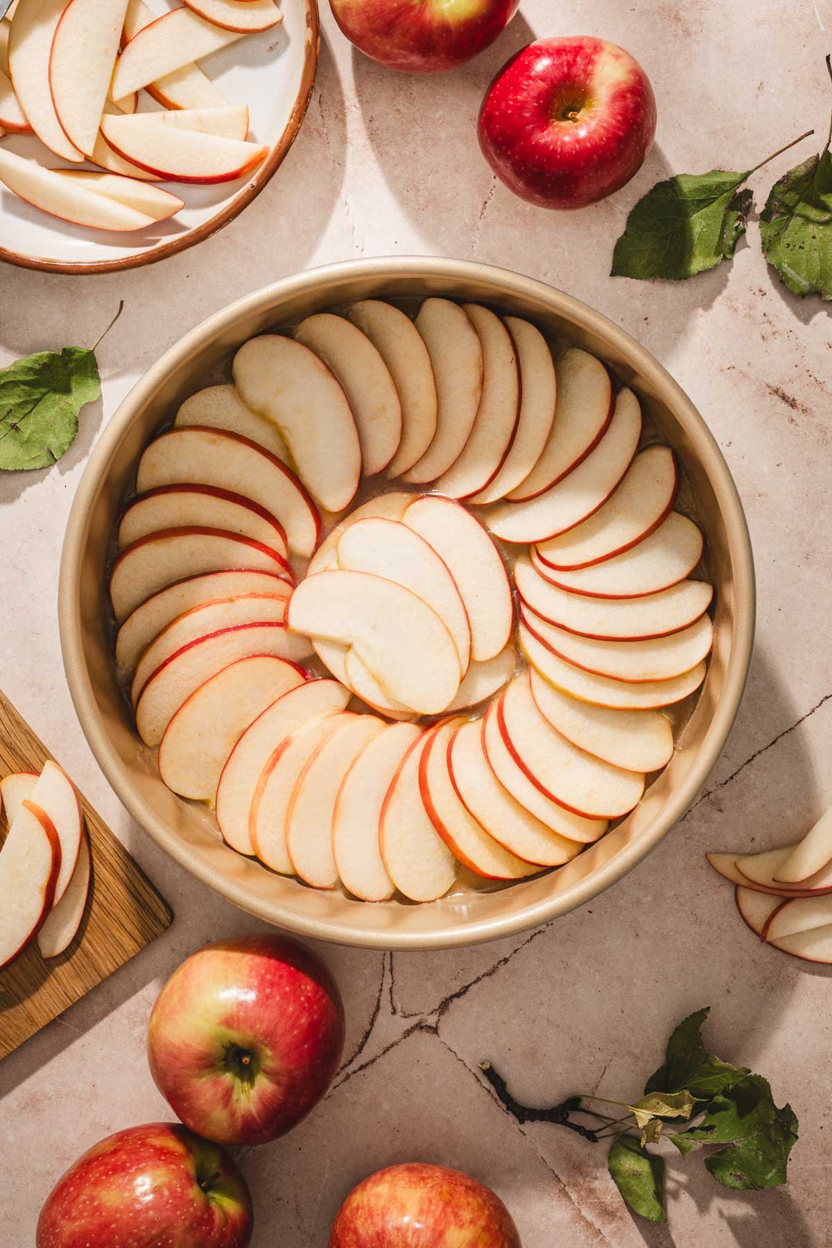 Thin red apple slices arranged in a spiral in a gold cake pan, ready for the batter.