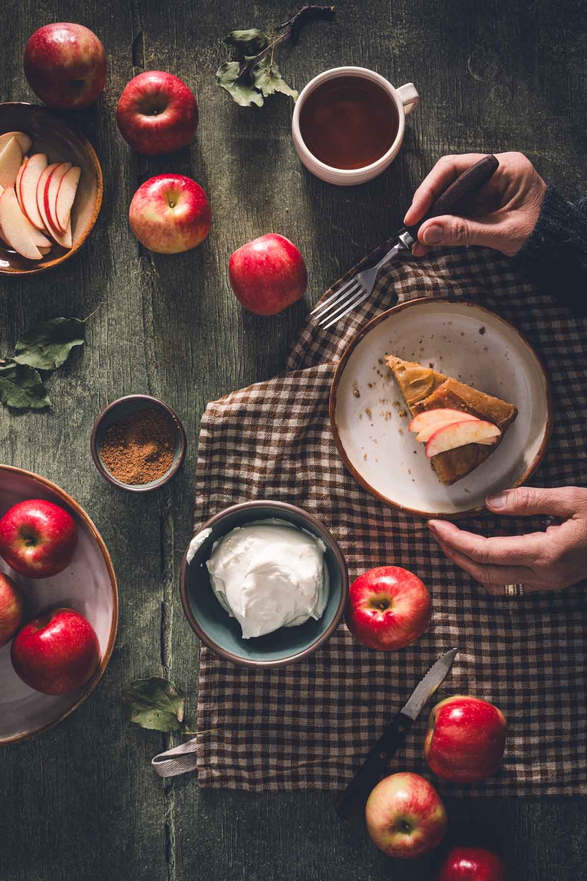 Hands with a fork about to dig into a slice of apple upside down cake topped with fresh apple slices.