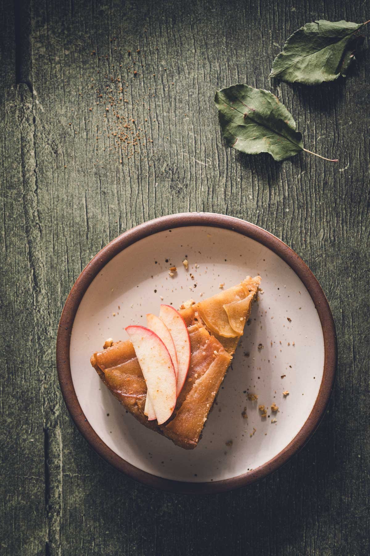 Slice of caramelized apple upside down cake topped with thin fresh apple slices on a speckled plate.