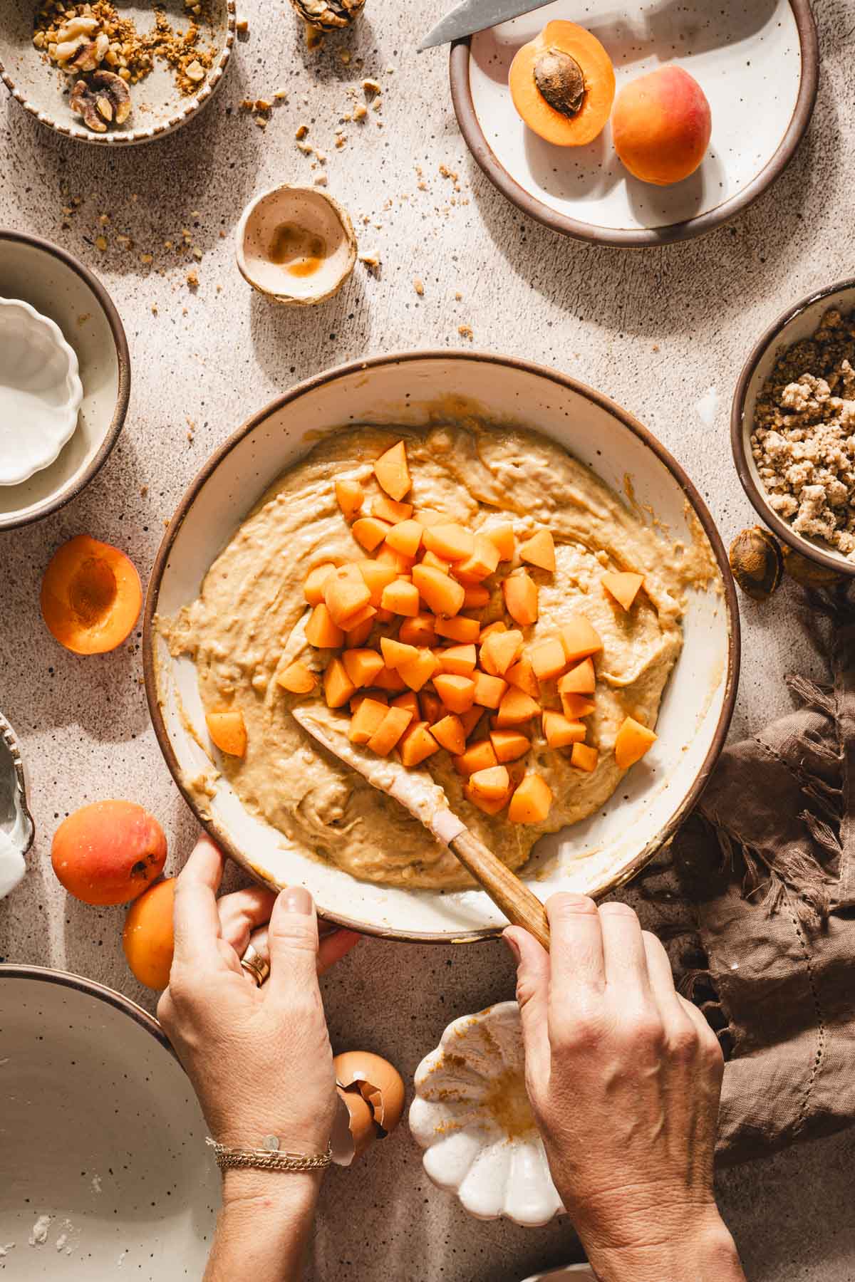 hands in frame mixing apricots into the batter