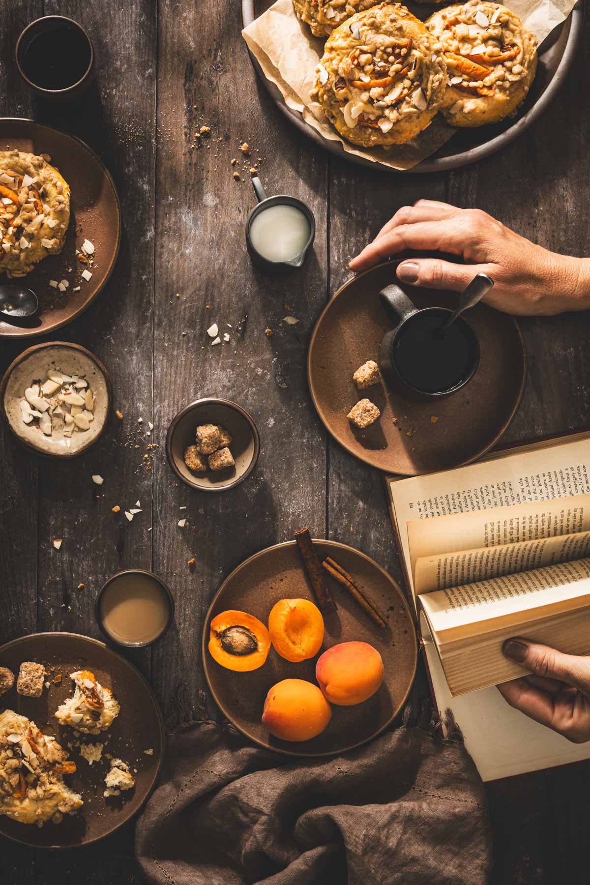 wooden backdrop, hands in frame holding a cup with coffee, book