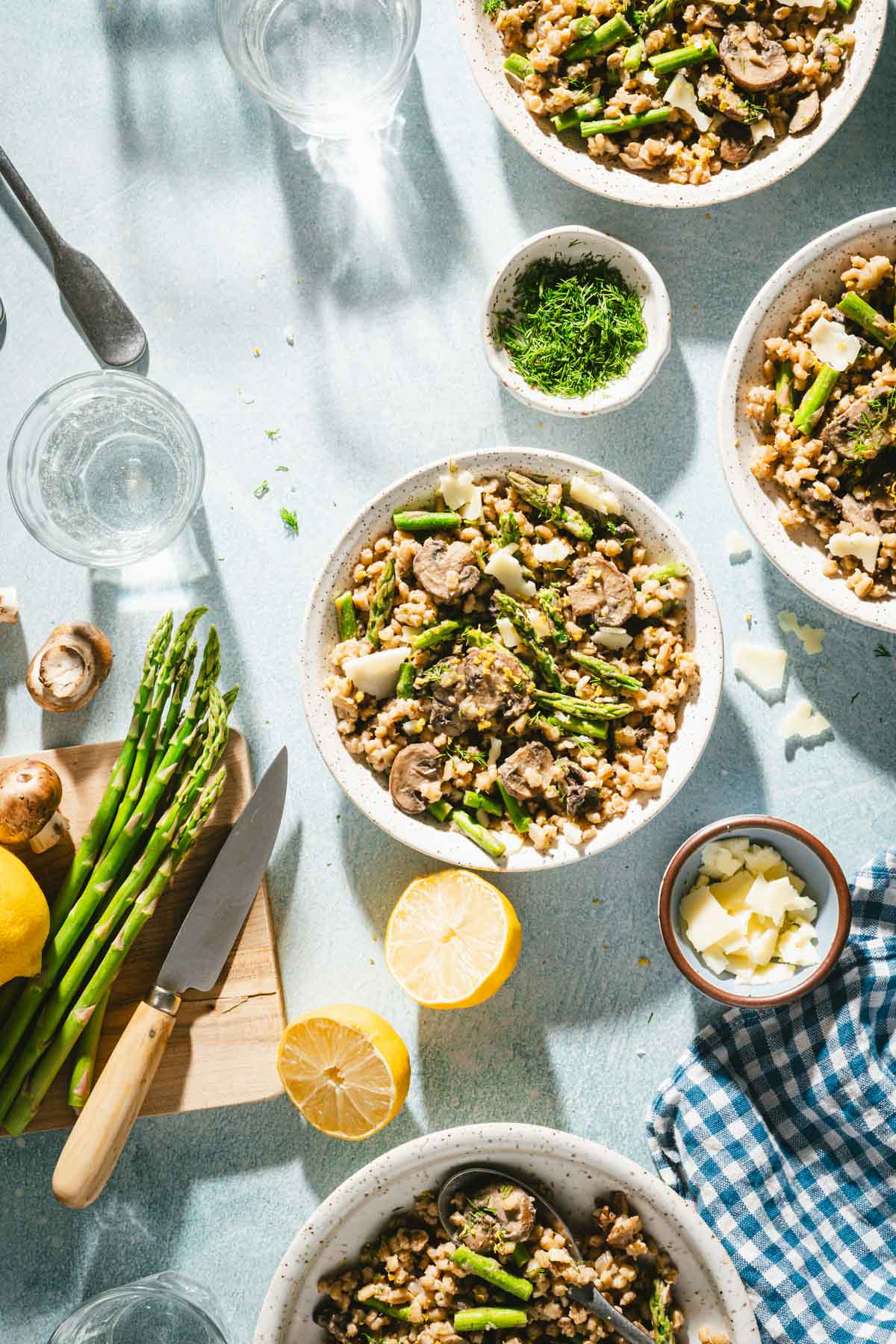 various serving dishes with risotto, cutting board with asparagus and lemon