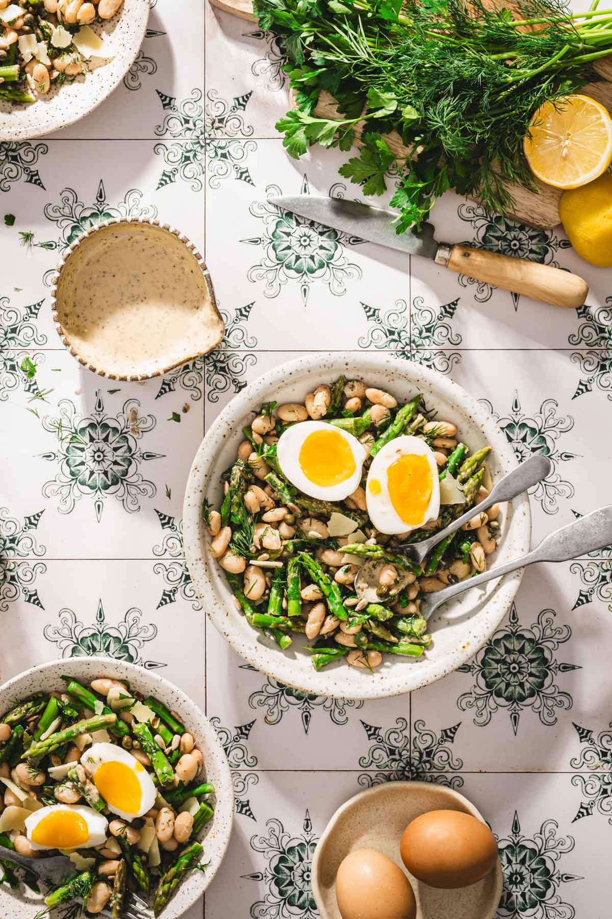 various bowls with the asparagus salad, cutting board with greens