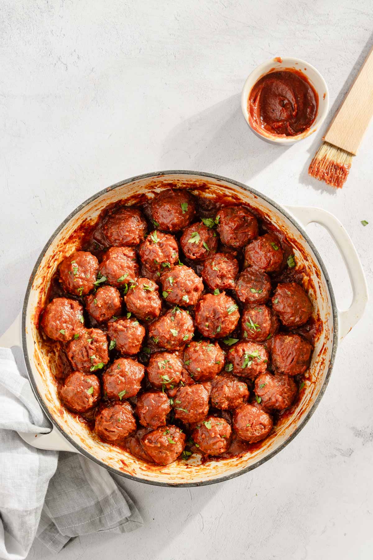 cooked bbq meatballs in a sauce pan, small dish with bbq sauce and a sauce brush, smoked meatball recipe