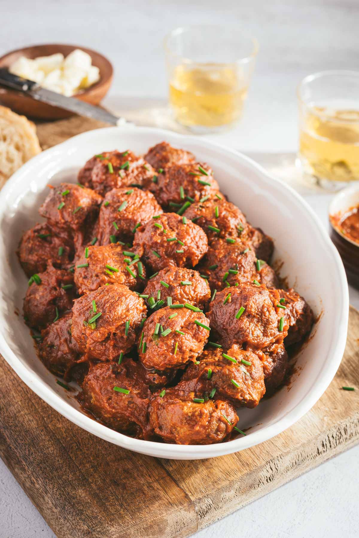 BBQ Meatballs on a sesrving platter, slices of bread, two glasses, dish with bbq sauce and a sauce brush