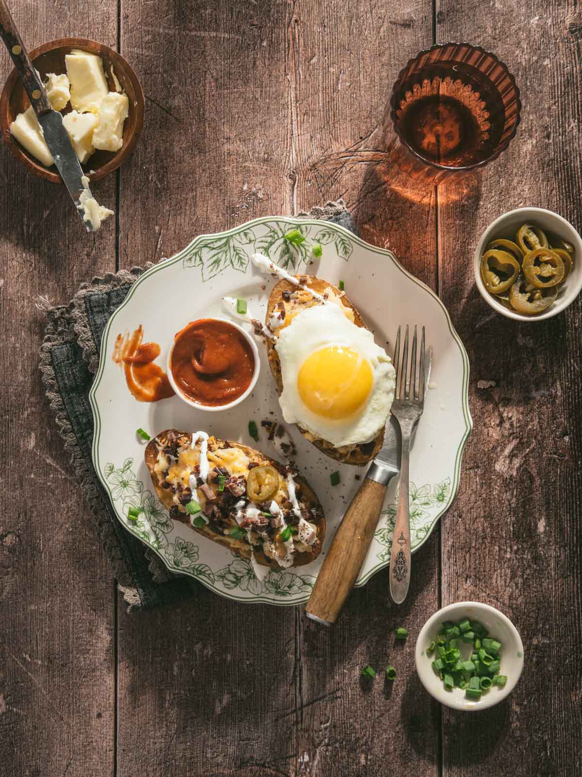 halves of baked potato served with chili , sunny side egg, bbq sauce, and other garnishes, glass of water