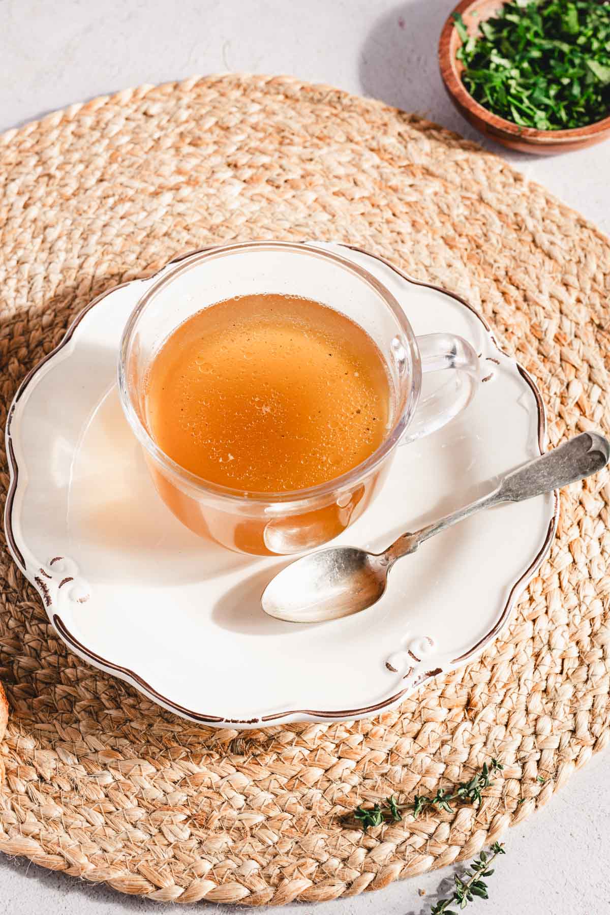 beef broth in a drinking glass, on a plate, spoon