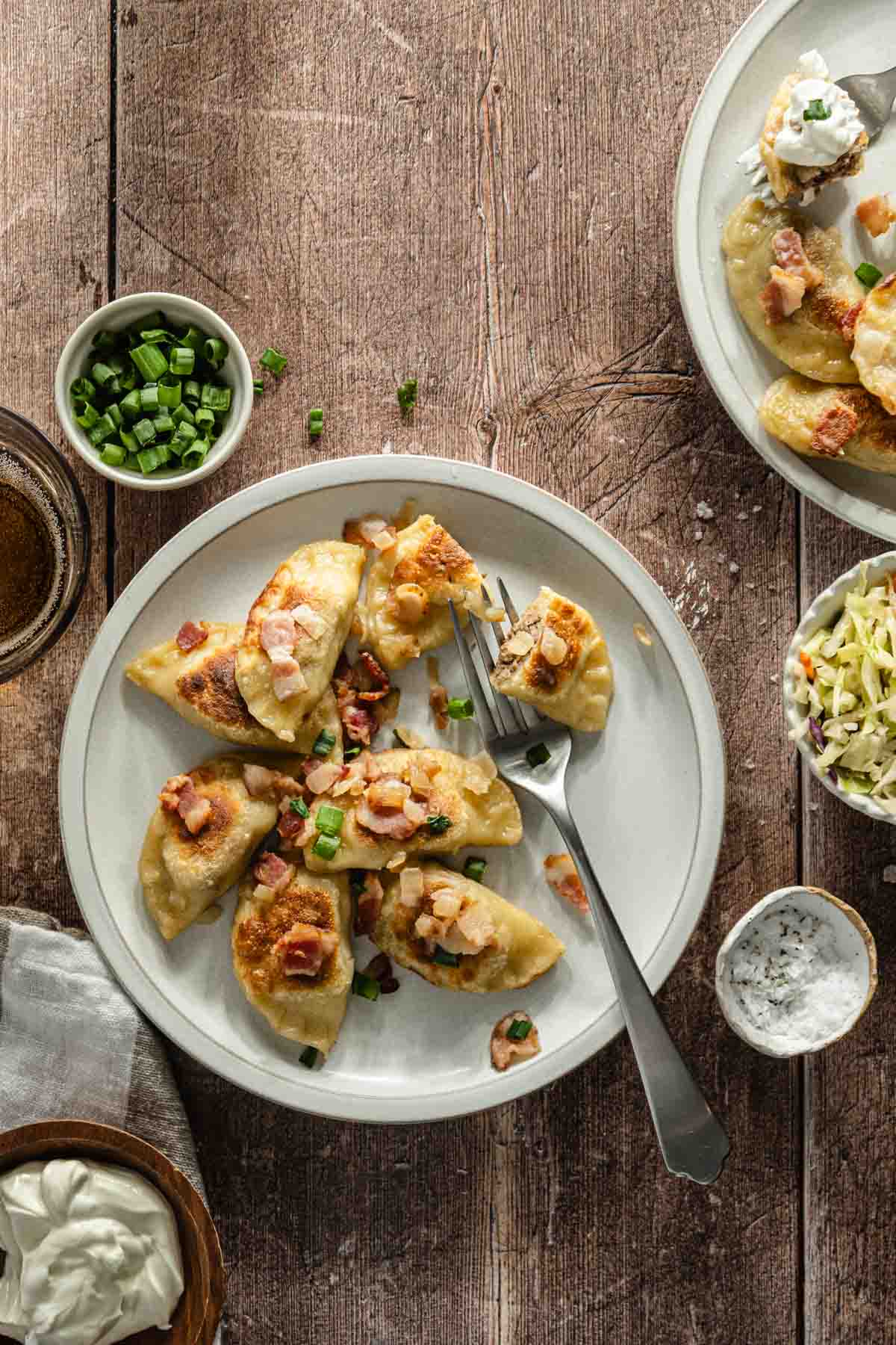 plates with cooked pierogis with bacon-onion topping and a side salad, glass of water