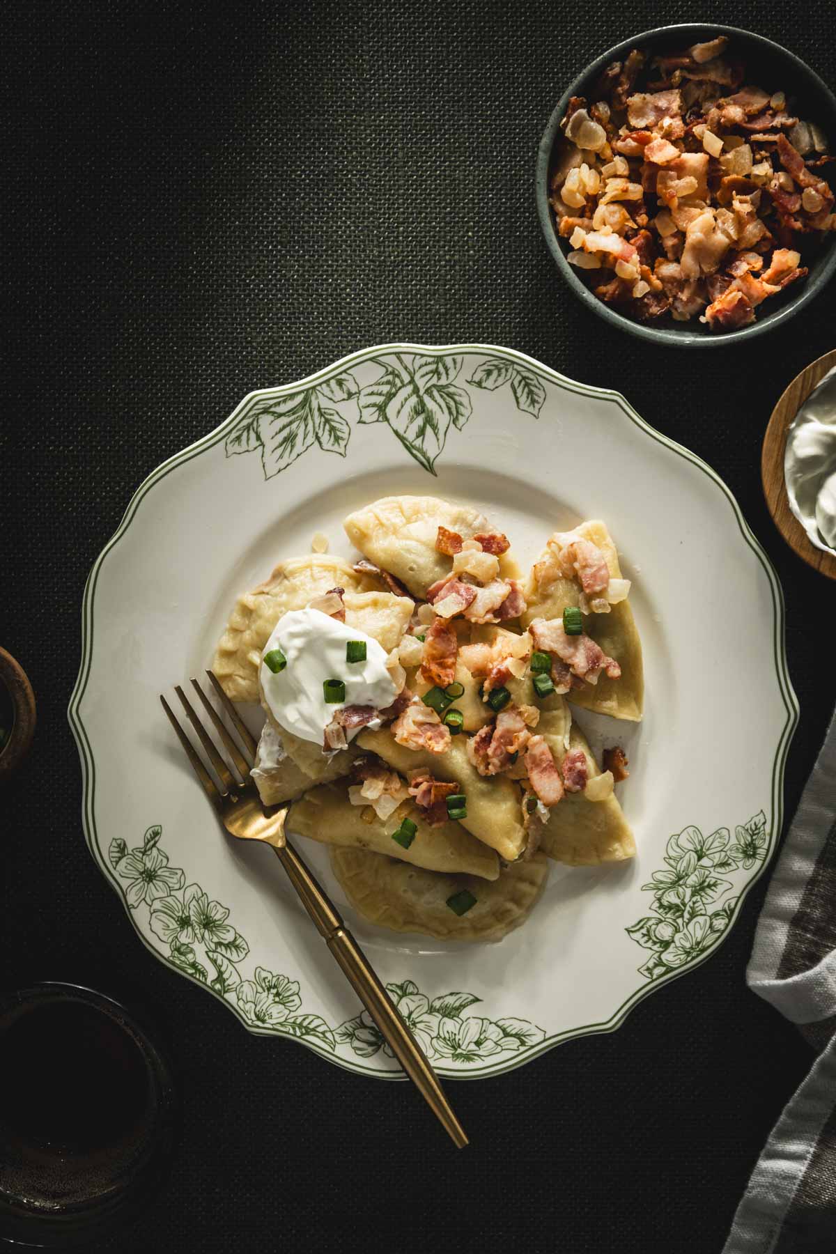 plate with cooked pierogis with bacon-onion topping and a dollop of sour cream