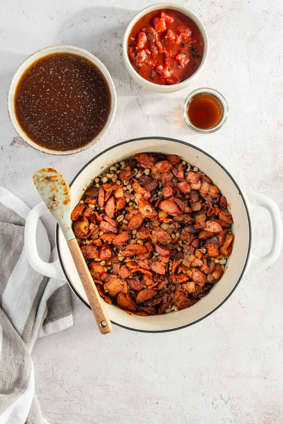 pot with black-eyed peas, bacon and sausage; two small bowls, one with broth, one with roasted tomato 