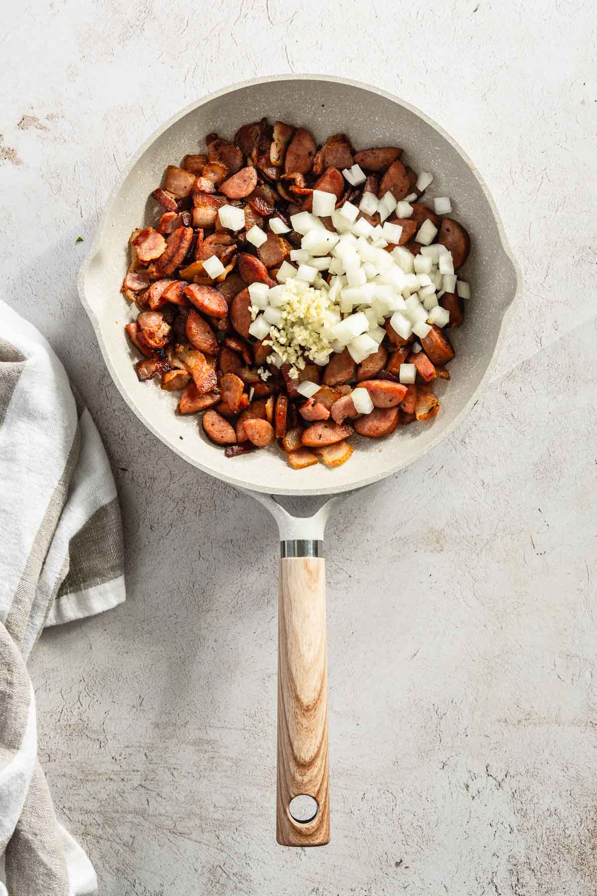 sausage and bacon on a frying pan, after cooking with added diced onion and garlic