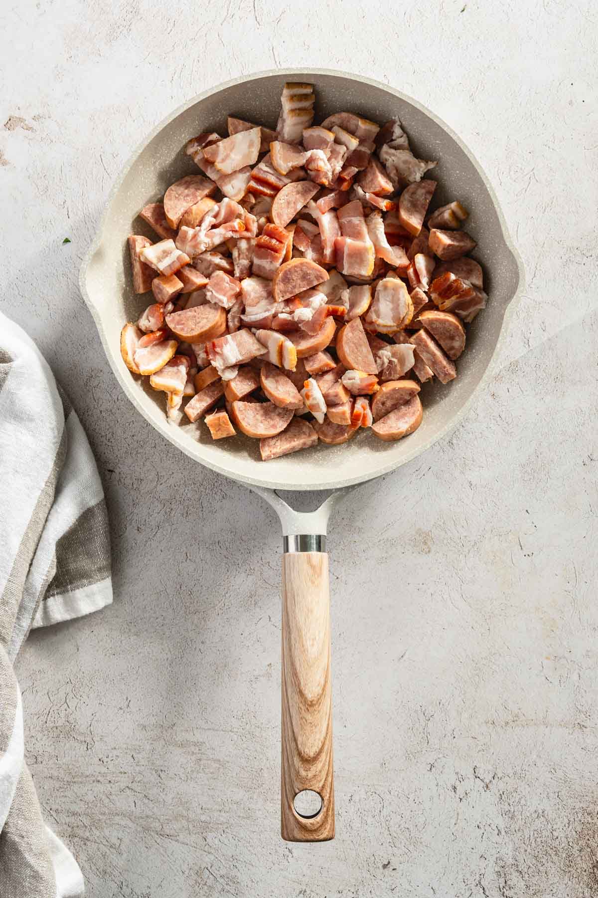 cut up sausage and bacon on a frying pan, before cooking