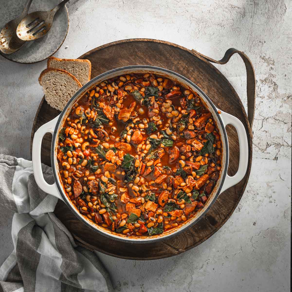 Black-Eyed Pea Stew in a saucepan, on a wooden serving board, piece of bread, napkin