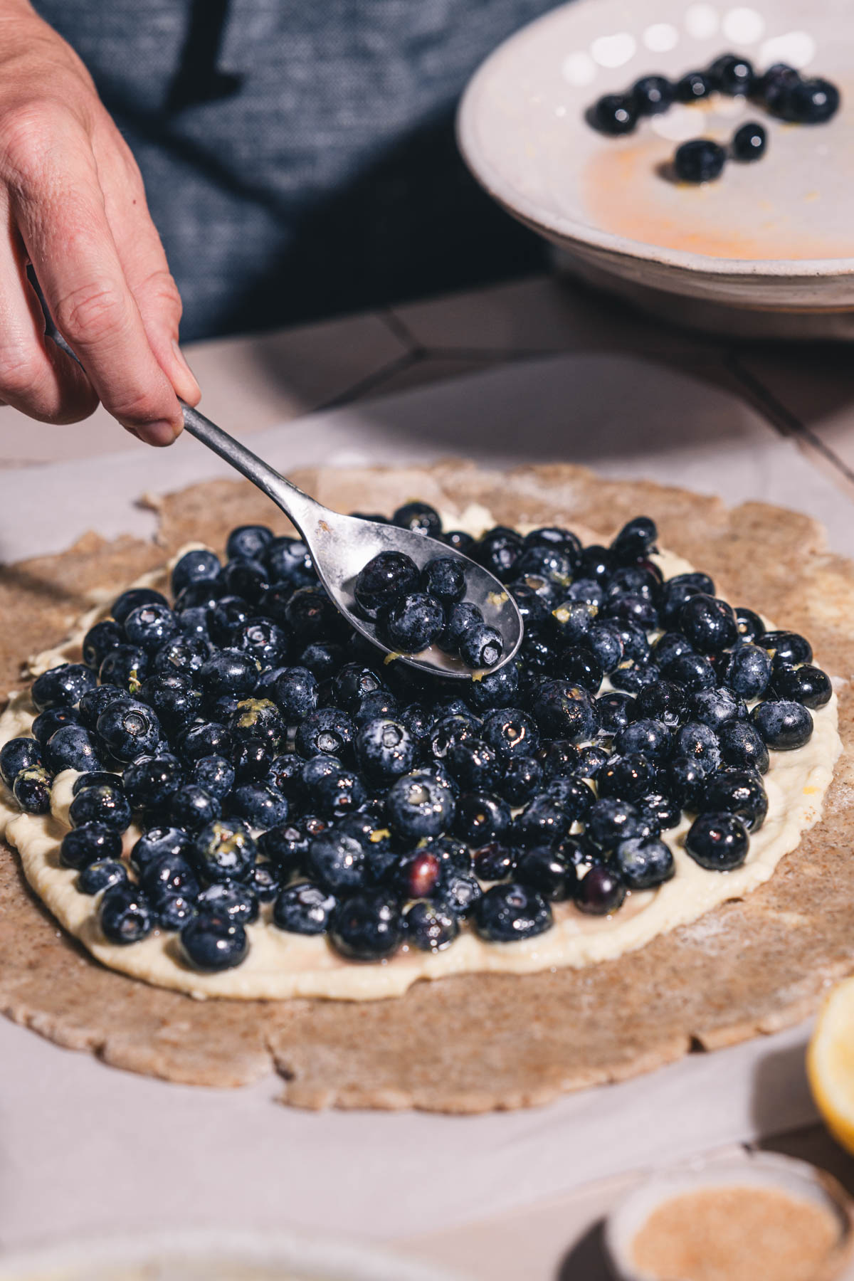 hands in frame holding spoon with blueberries over the galette crust