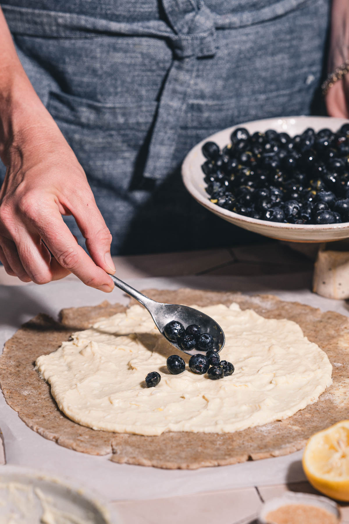 hands in frame holding spoon with blueberries over the galette crust
