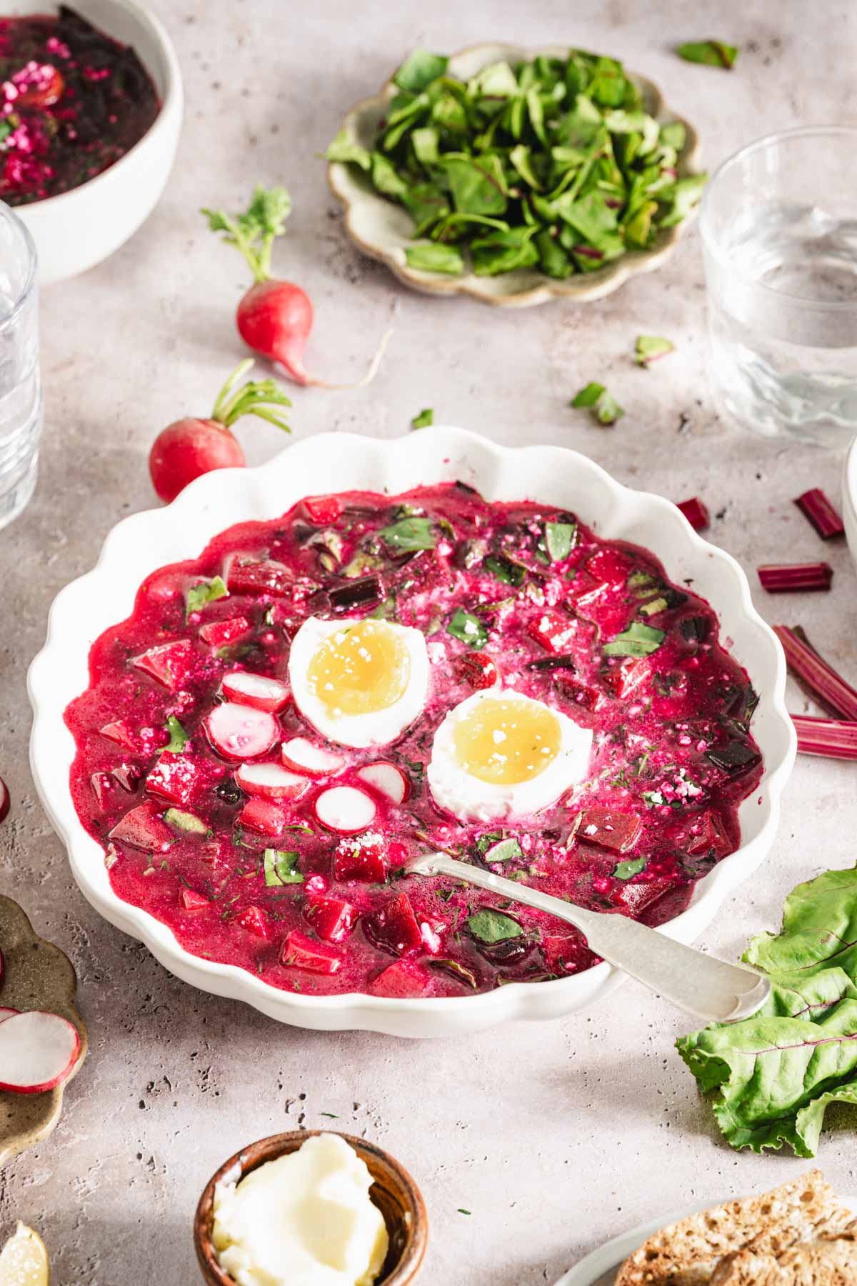 botwinka soup in a serving bowl, with hard boiled egg, radishes, dish with beet greens, butter