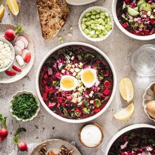 botwinka soup in a serving bowl, garnished with egg, cucumbers, feta cheese