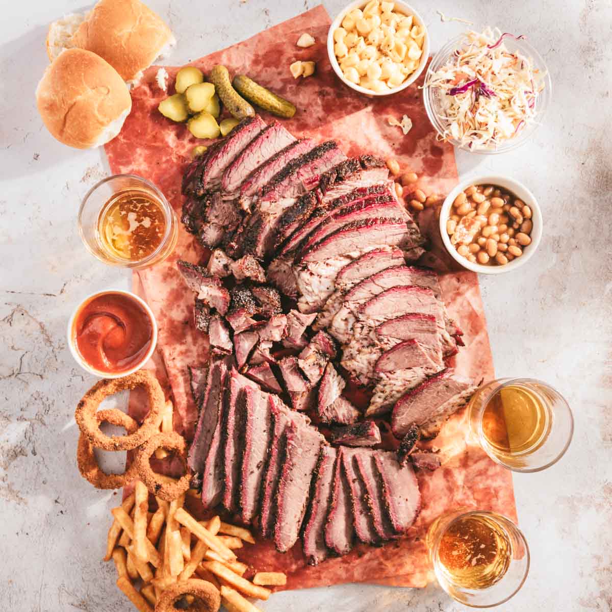 sliced smoked brisket on a butcher paper with different dishes with sides, glasses with beer