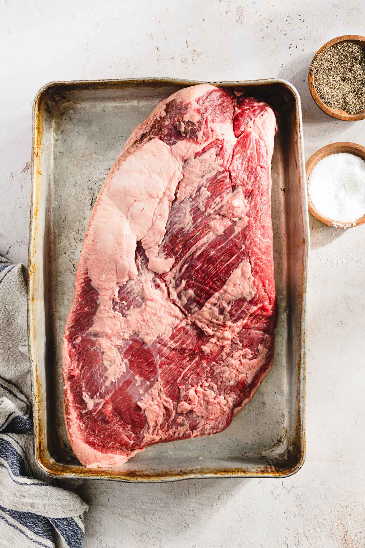 raw brisket on a baking sheet, salt pepper