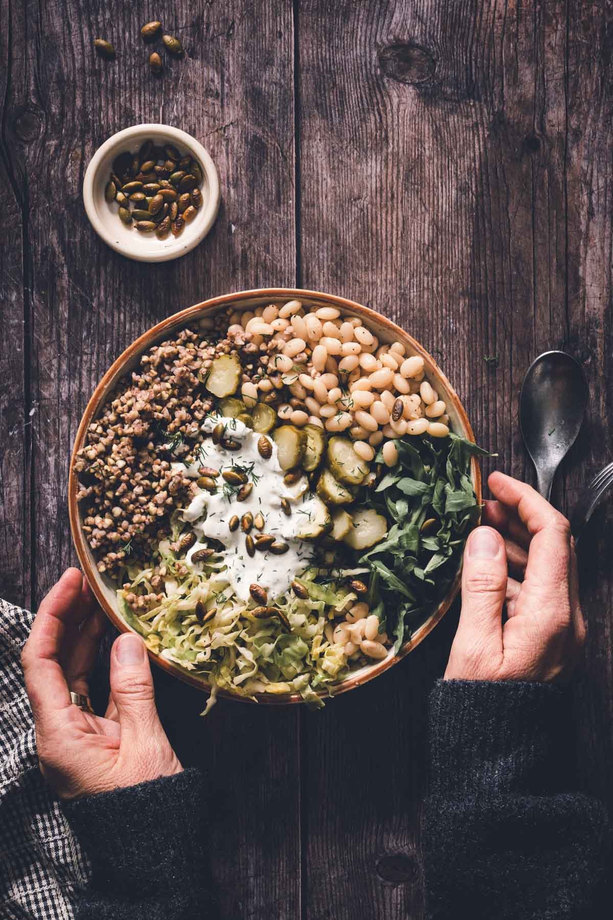 hands in frame holding buckwheat bean bowl in a serving bowl