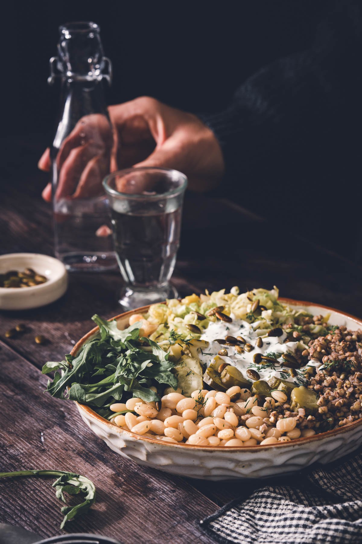 hands in frame holding glass with water, buckwheat bean bowl in a serving bowl