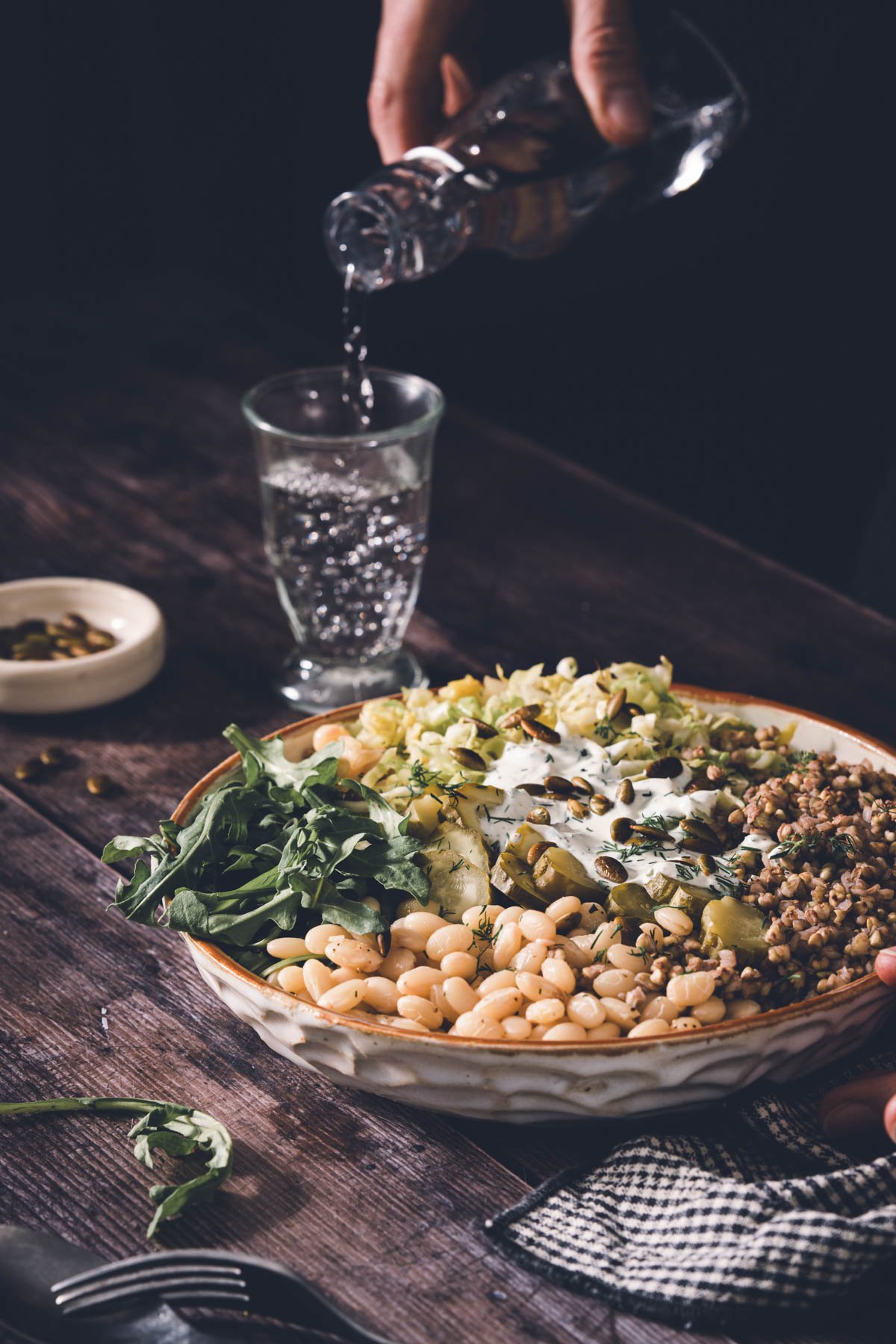 hands in frame pouring water into a glass, buckwheat bean bowl in a serving bowl
