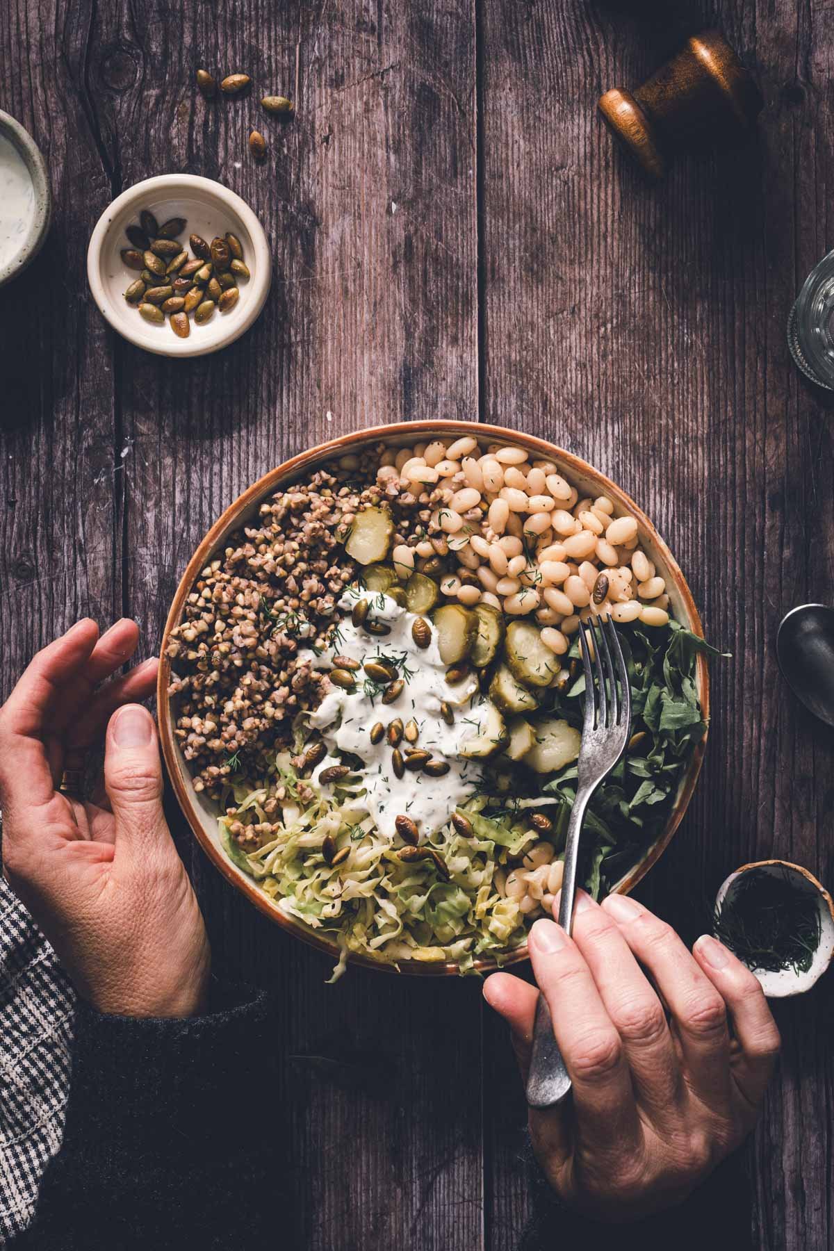 hands in frame holding fork over buckwheat bean bowl in a serving bowl