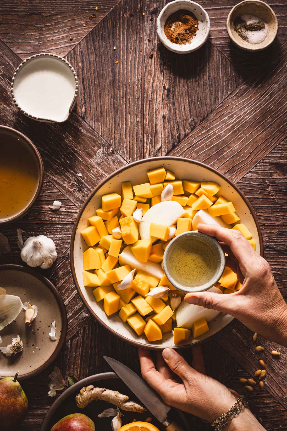hands in frame adding oil to the bowlwith squash and onio