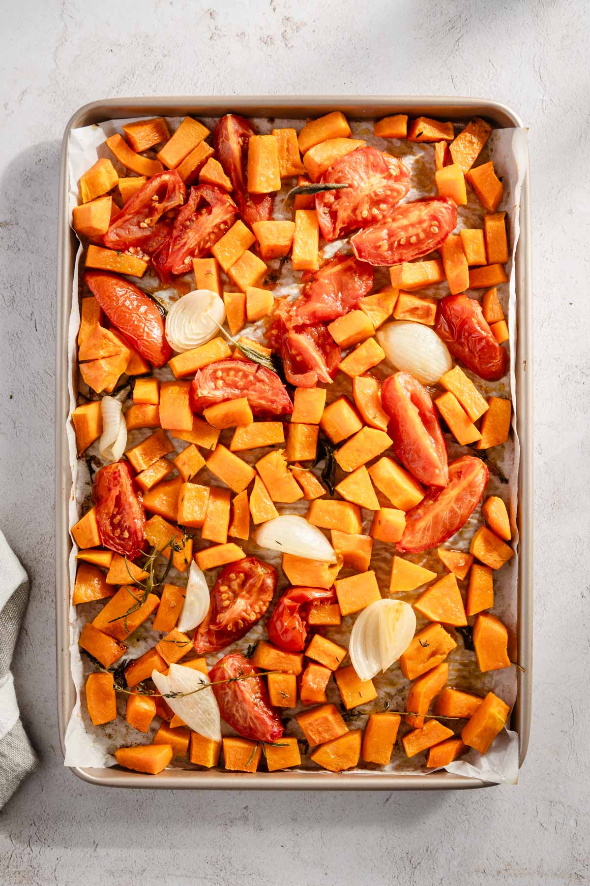 roasted tomatoes, butternut, onions and herbs on a baking sheet