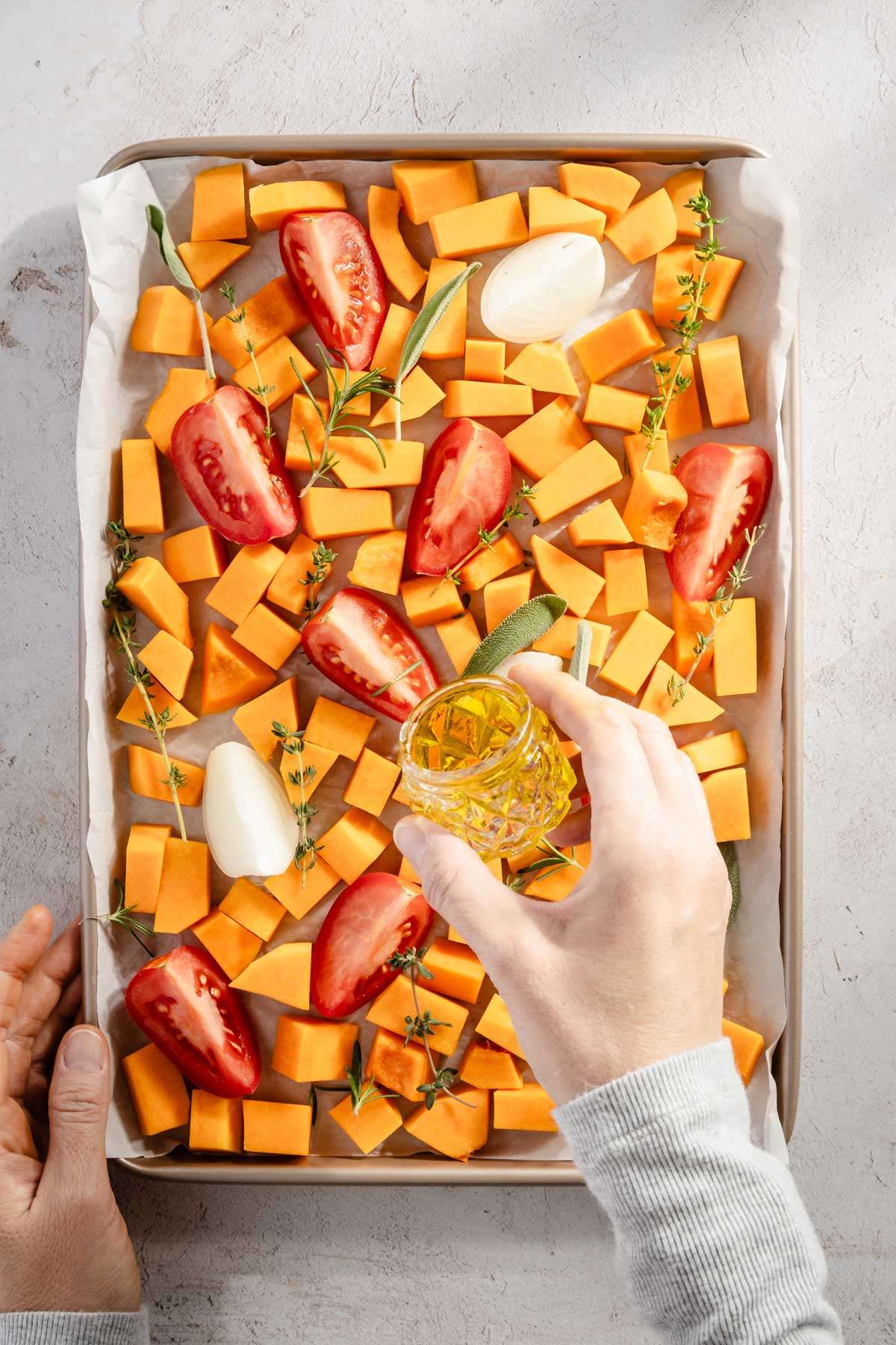 hand in frame, drizzling olive oil over the cut up veggies on a baking sheet