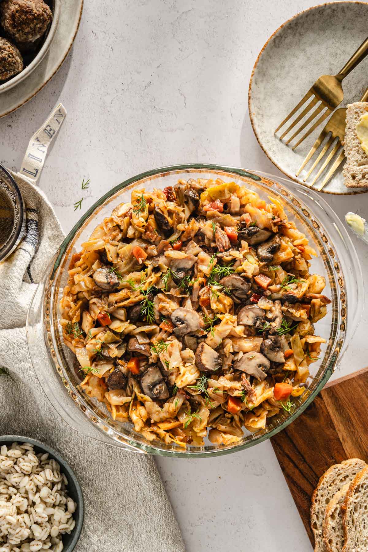 cooked smoked cabbage in a glass serving dish, napkin, slices of bread; bowl with meatballs, plate with forks, bowl with barley