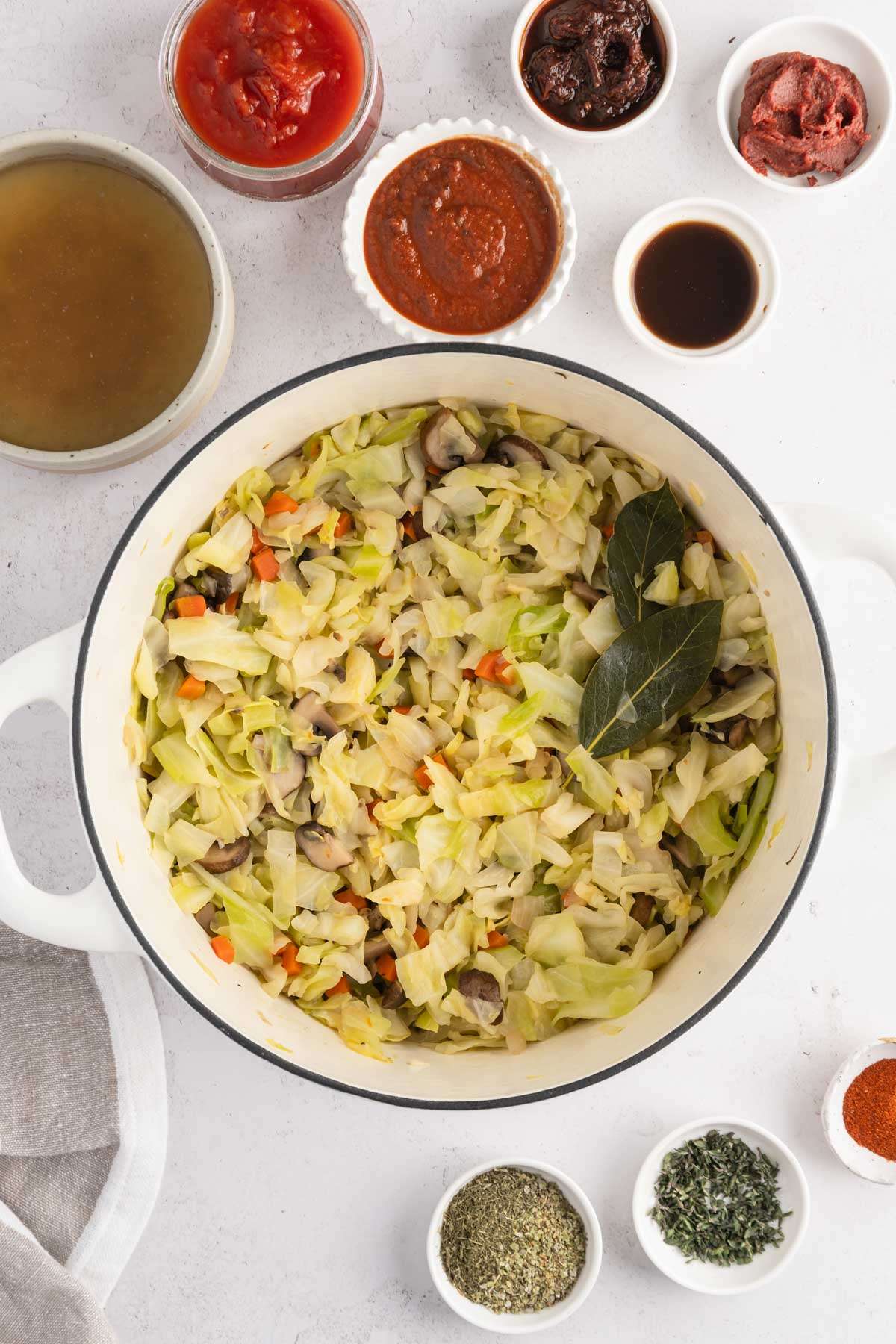 veggies mixed in the cooking pan, small bowls with other ingredients, broth, paste, etc