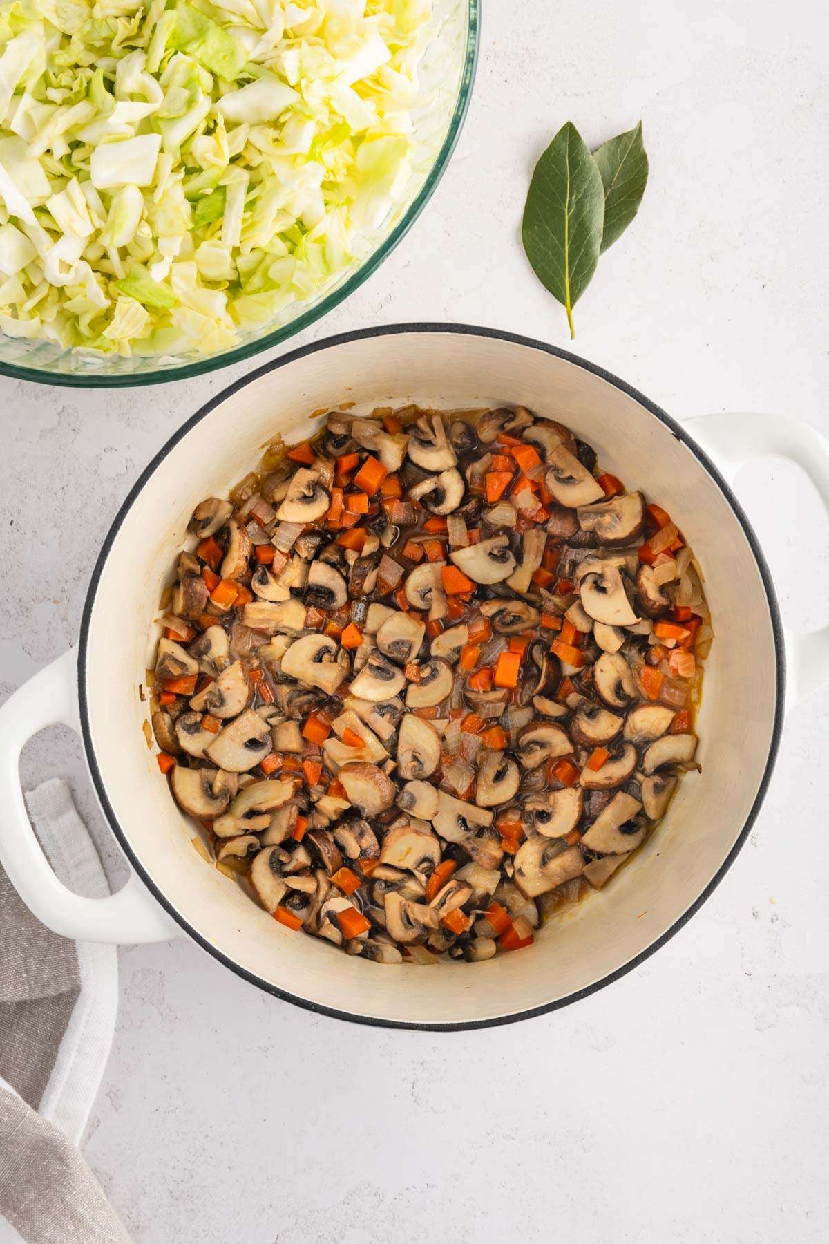 cooking pan with cooked mushrooms, onion and carrots, bowl with chopped cabbage