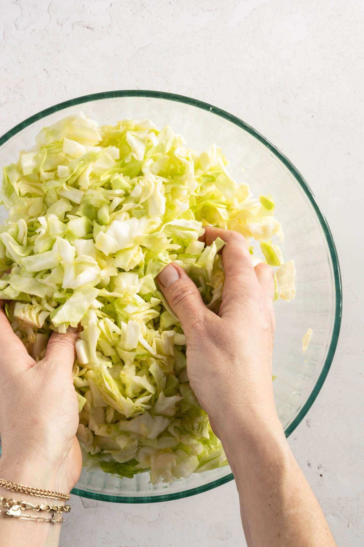 chopped cabbage in a glass bowl, hands in frame mixing the cabbage with salt