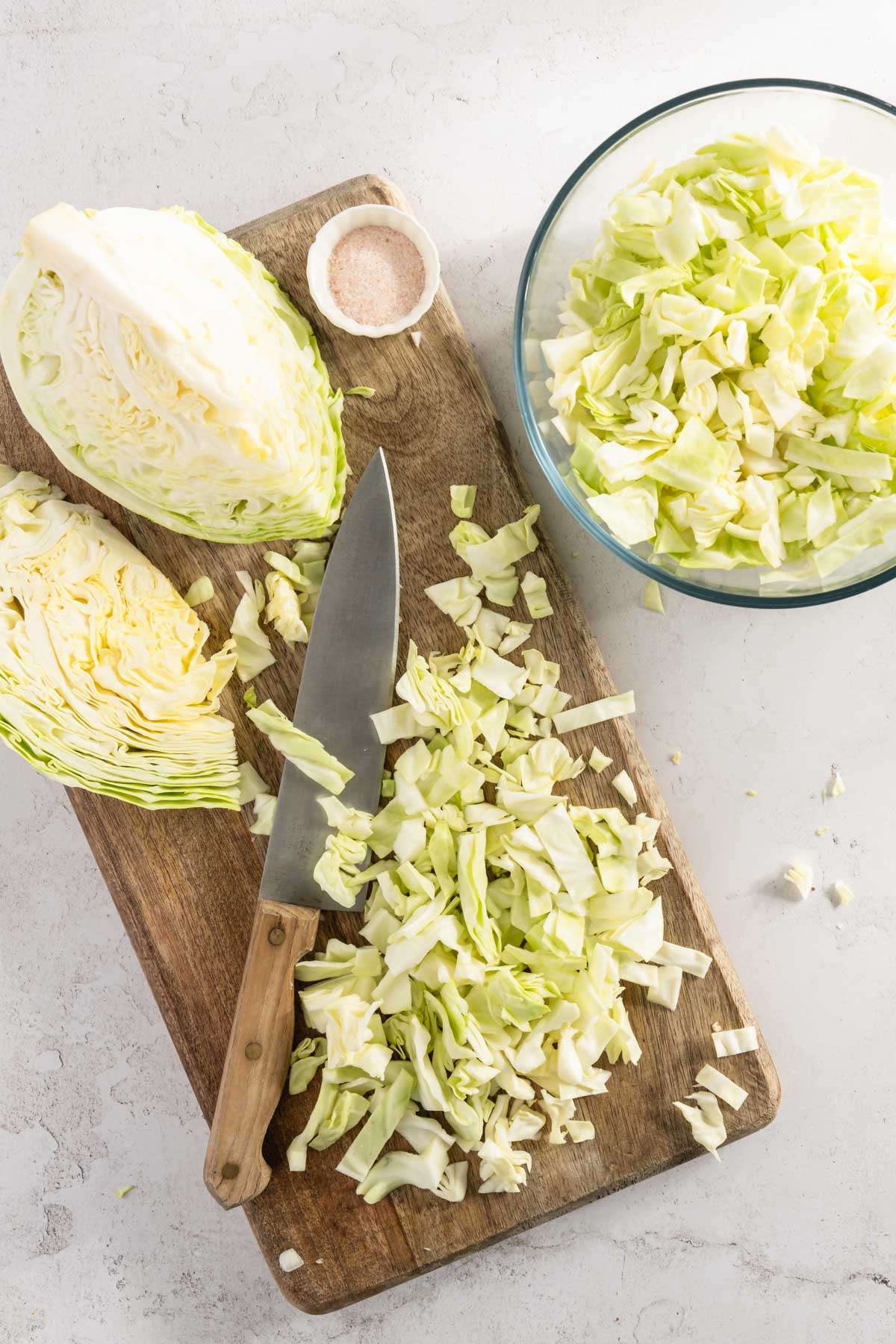 white cabbage on a chopping board, bowl with chopped cabbage, knife