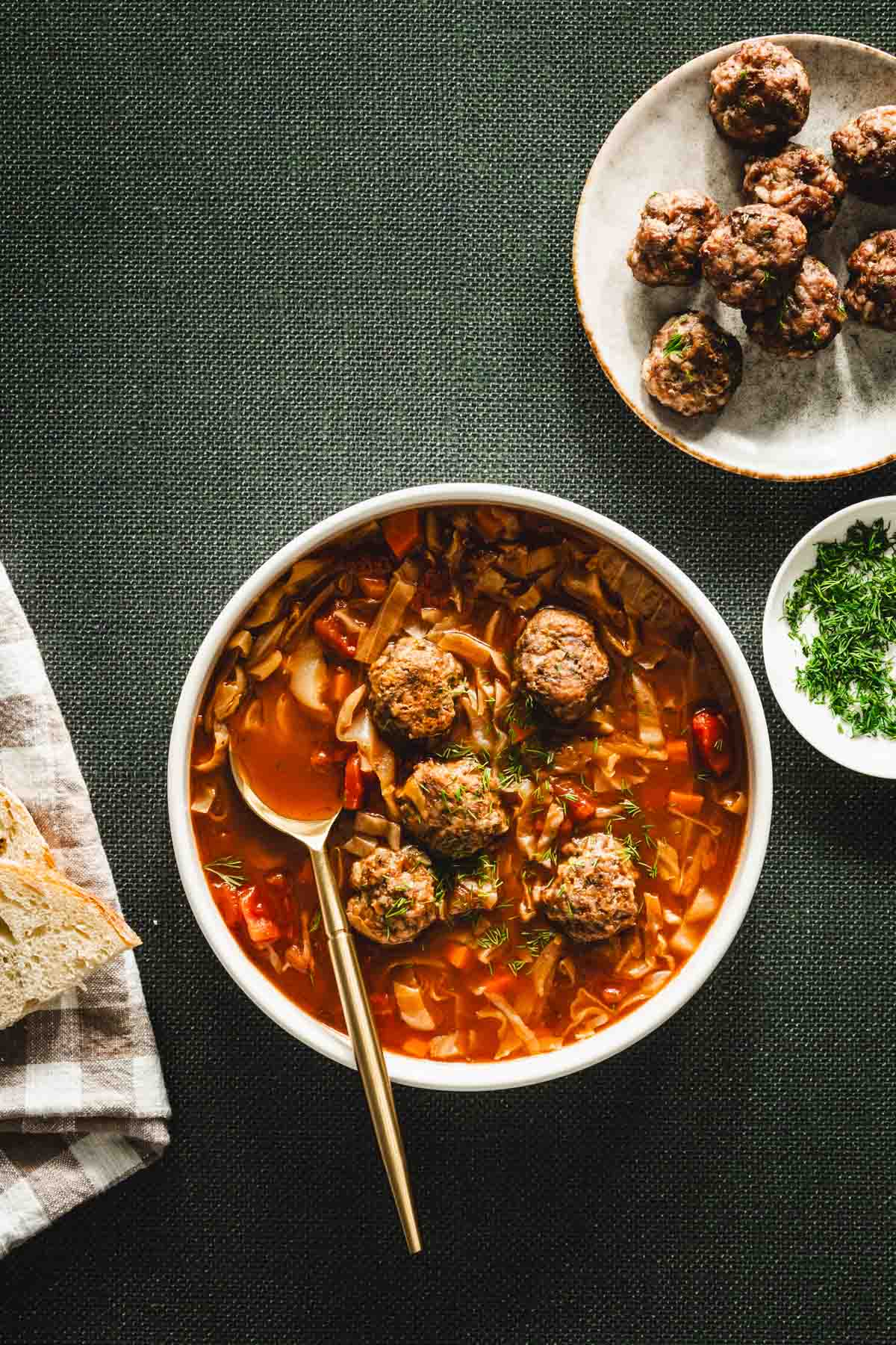 green background, bowl with cabbage soup, meatballs on the plate, dish with fresh dill, napkin, slices of bread