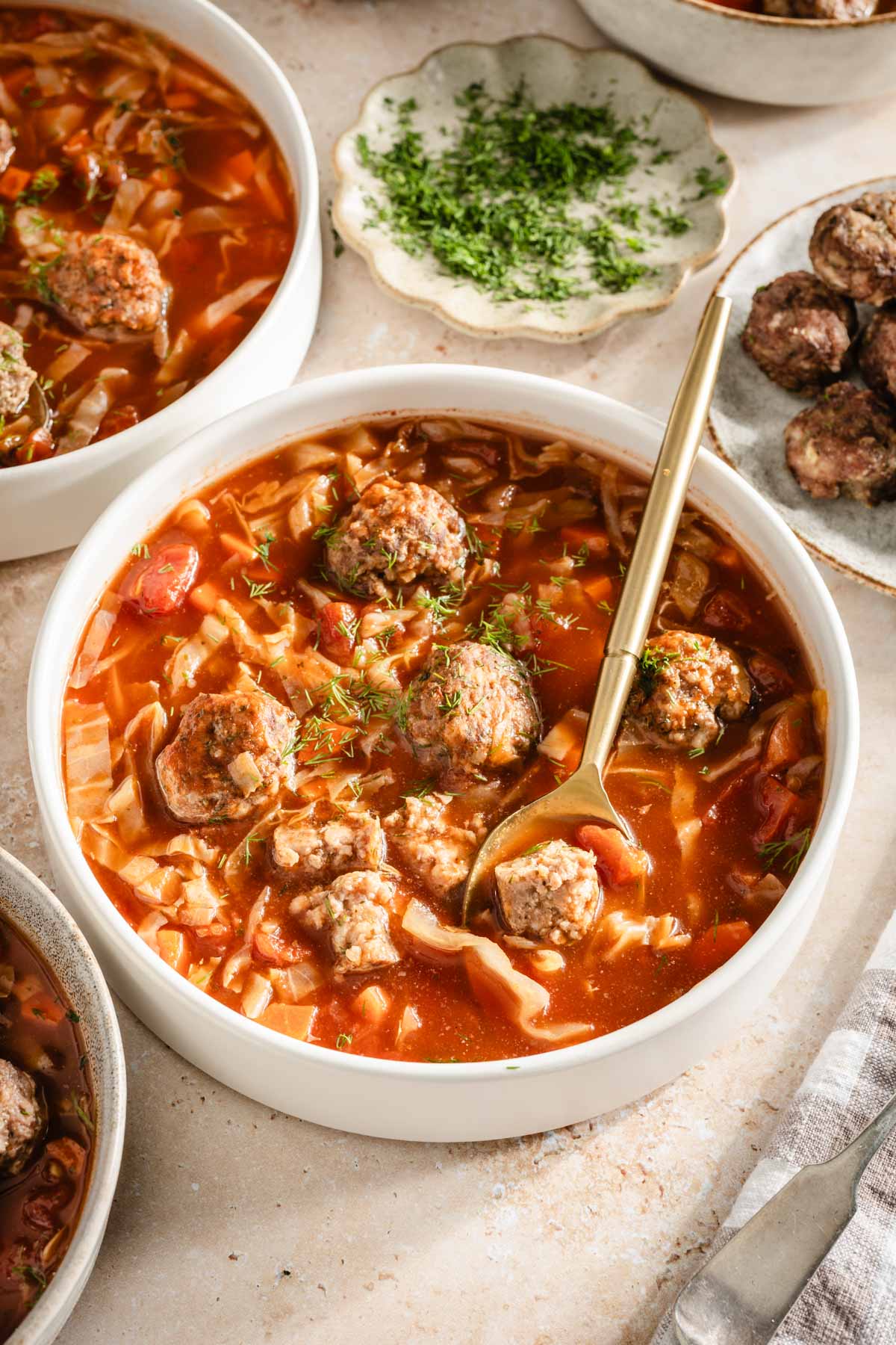 Cabbage soup served in bowls, meatballs on the side, bread knife, bread basket, dish with fresh dill