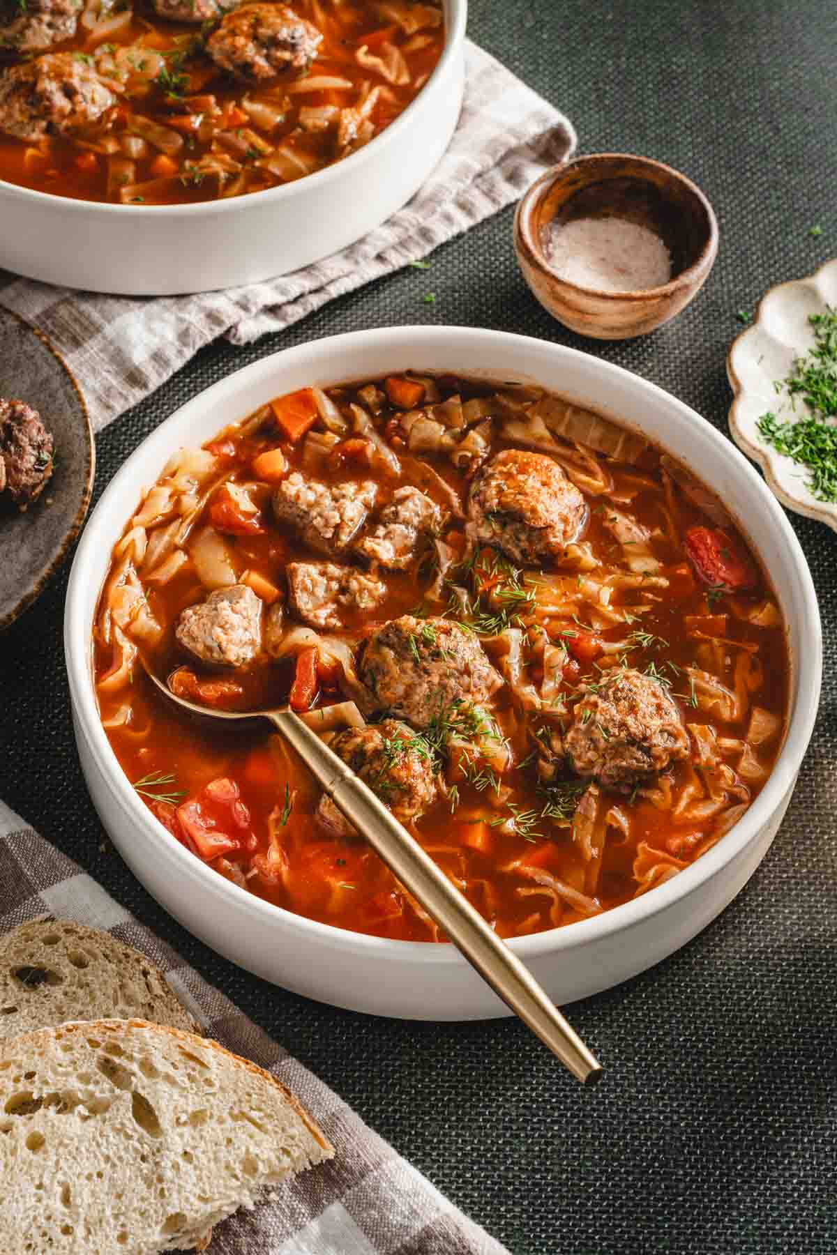 green background, bowl with cabbage soup, meatballs on the plate, dish with fresh dill, napkin, slices of bread, spoon in the soup