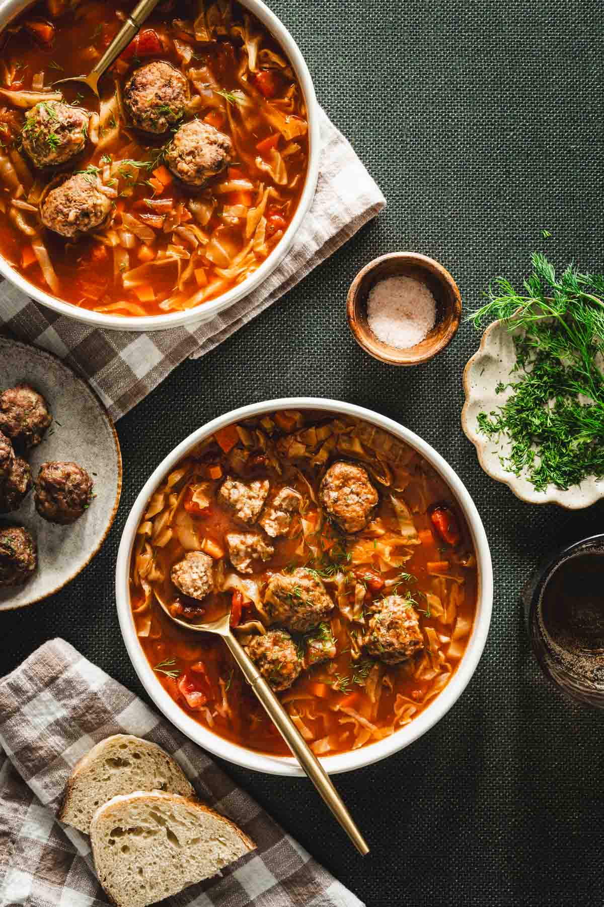 green background, bowl with cabbage soup, meatballs on the plate, dish with fresh dill, napkin, slices of bread