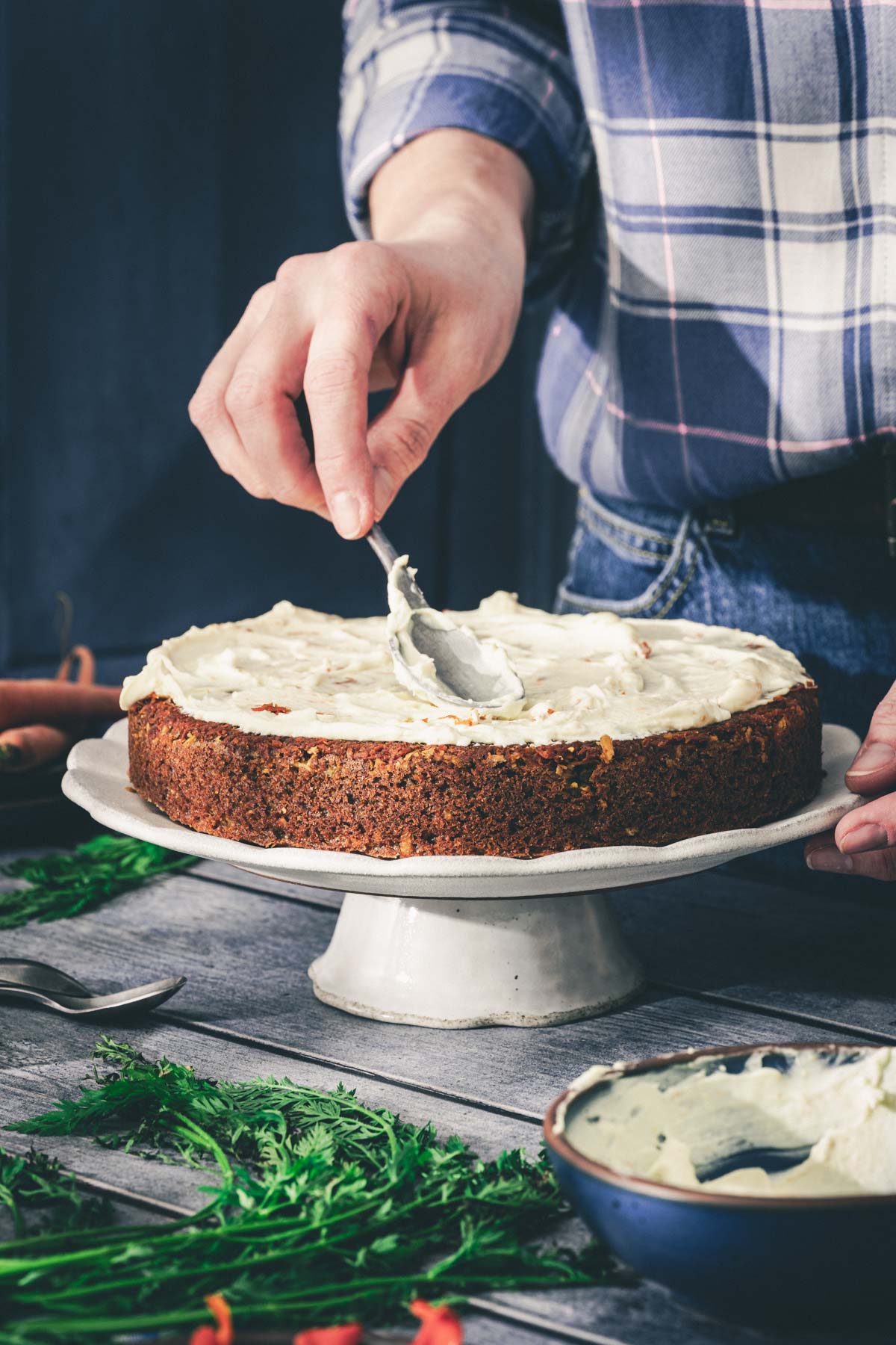 hands in frame holding spoon with cream cheese frosting over the cake