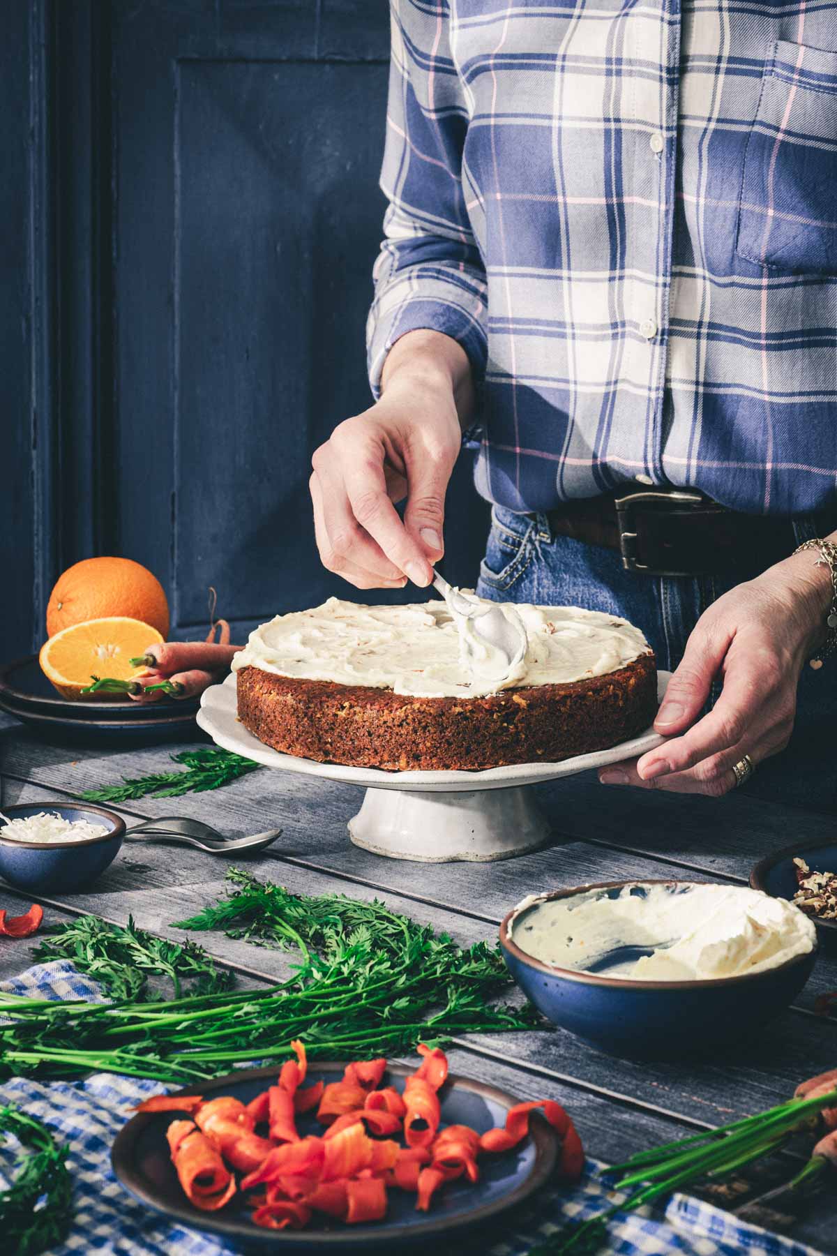 hands in frame holding spoon with cream cheese frosting over the cake