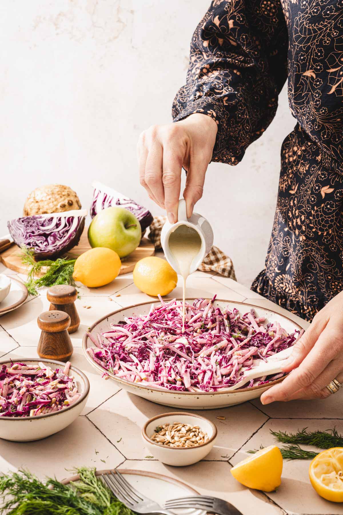 hands in frame holding pourer and pouring dressing over the salad
