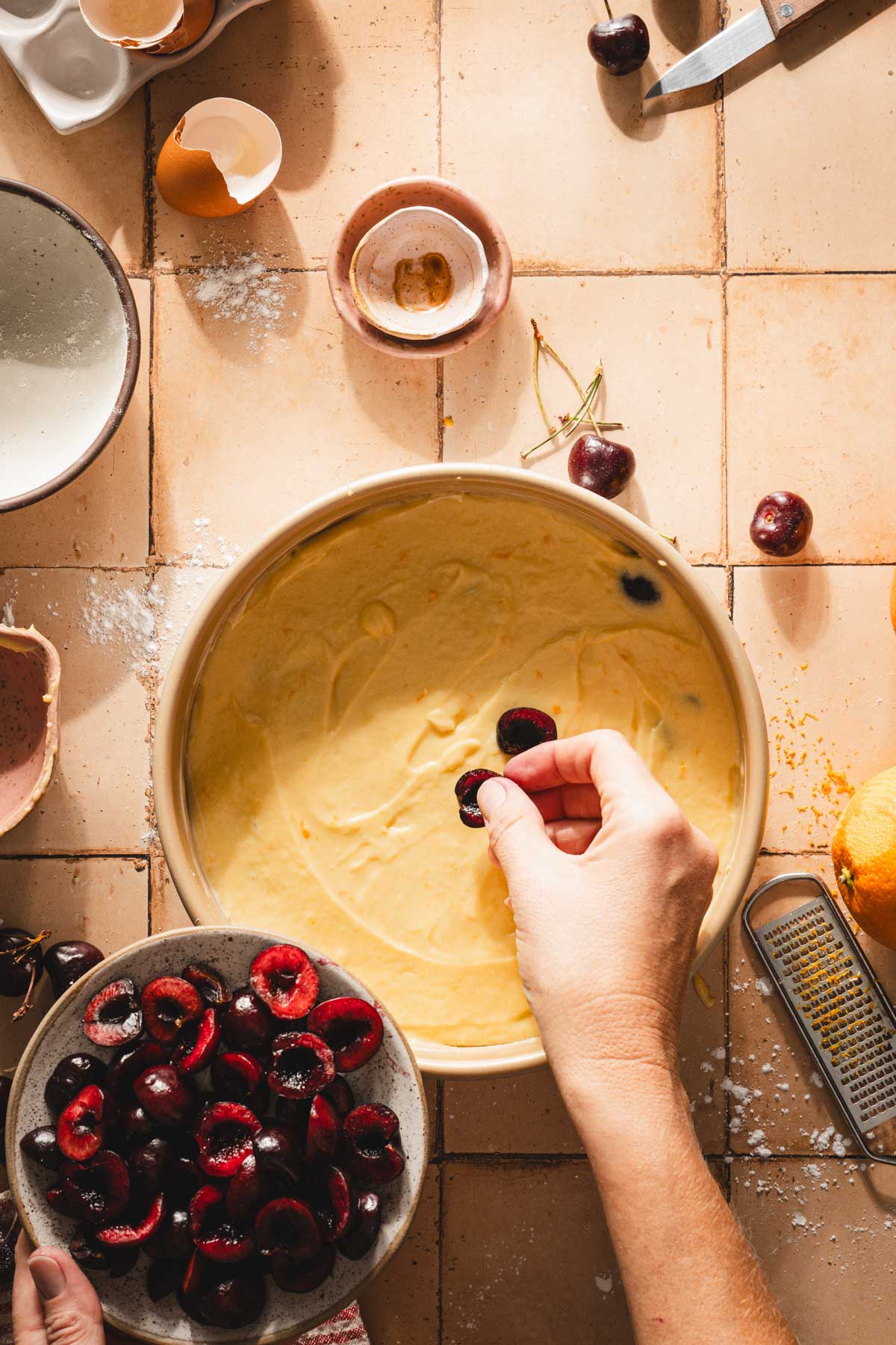 hands in frame adding cherries on top of the cake batter